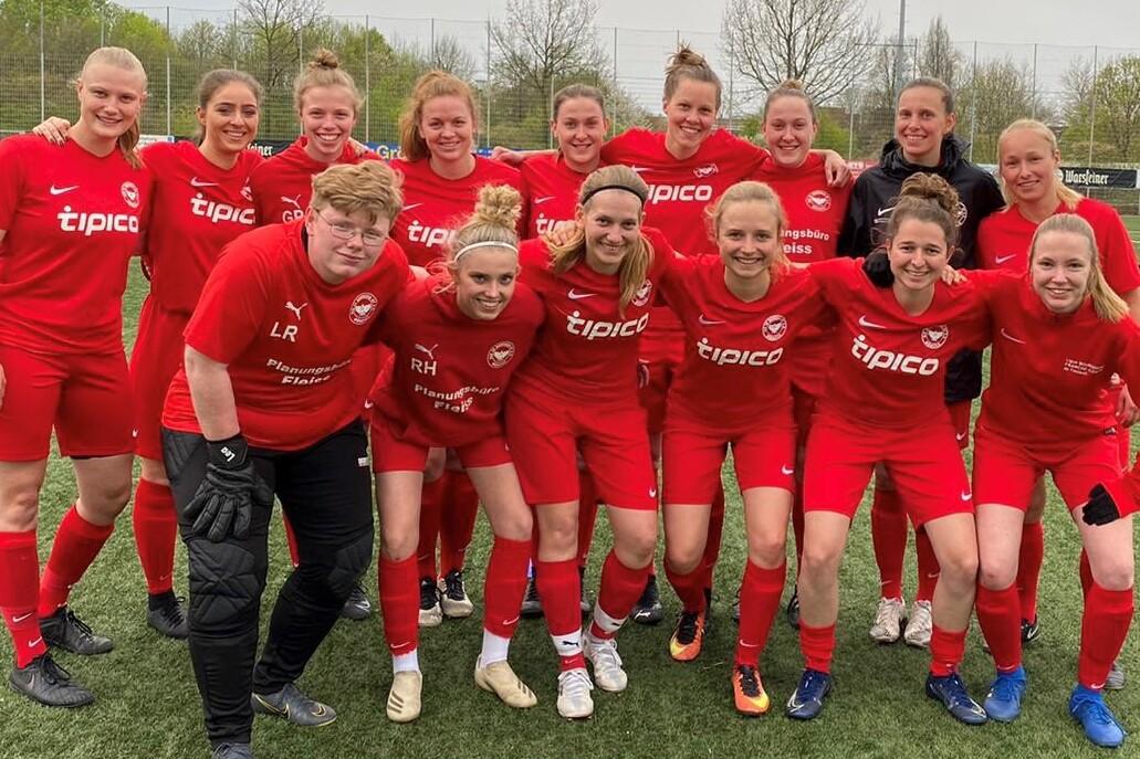 Gruppenfoto von 16 Fu&szlig;ballspielerinnen in roten Trikots auf einem Rasenplatz, smiling und in sportlicher Pose.