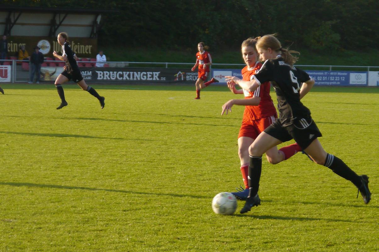 Fu&szlig;ballspiel mit Spielerinnen in roten und schwarzen Trikots, eine Spielerin dribbelt den Ball auf dem gr&uuml;nen Rasen.