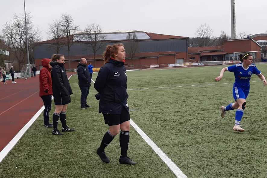Spielszene auf einem Fu&szlig;ballfeld mit Trainerin und Spielerinnen in blauen Trikots, Wechsel an der Seitenlinie.