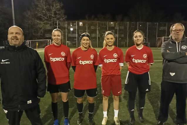 F&uuml;nf Fu&szlig;ballspielerinnen in roten Trikots stehen auf einem Sportplatz bei Nacht, zwei Trainer daneben.