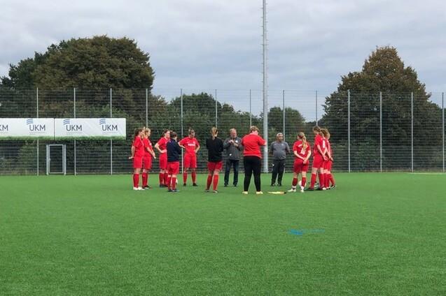 Eine Gruppe von Fu&szlig;ballspielern in roten Trikots versammelt sich auf einem Kunstrasenfeld zur Besprechung.