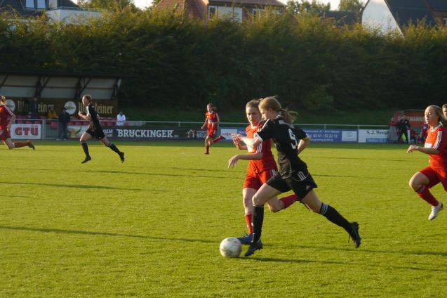 Fu&szlig;ballspiel mit Spielerinnen in roten und schwarzen Trikots, eine Spielerin dribbelt den Ball auf dem gr&uuml;nen Rasen.