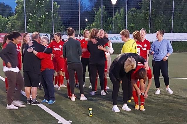 Gruppenszene von Fu&szlig;ballspielerinnen in roten Trikots, die sich auf einem Platz umarmen und feiern.