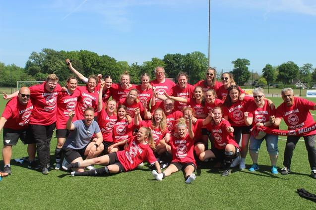 Gruppenshot eines begeisterten Frauenfu&szlig;ballteams in roten Shirts, das auf einem Platz feiert und jubelt.