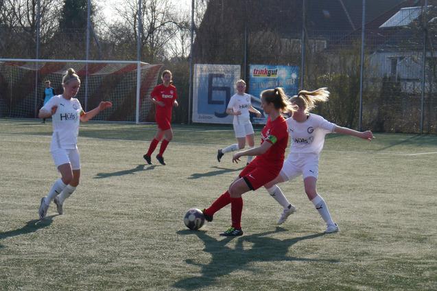 Zwei Fu&szlig;ballspielerinnen in roten und wei&szlig;en Trikots k&auml;mpfen um den Ball auf einem Kunstrasenplatz.