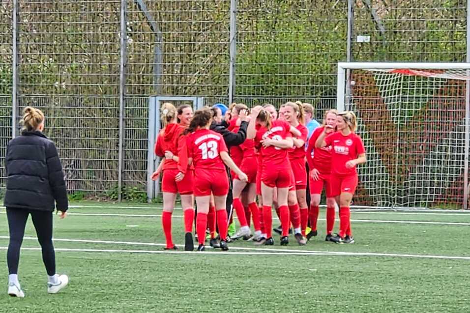 Gruppe junger M&auml;dchen in roten Fu&szlig;balltrikots feiert auf dem Spielfeld gemeinsam einen Torerfolg.