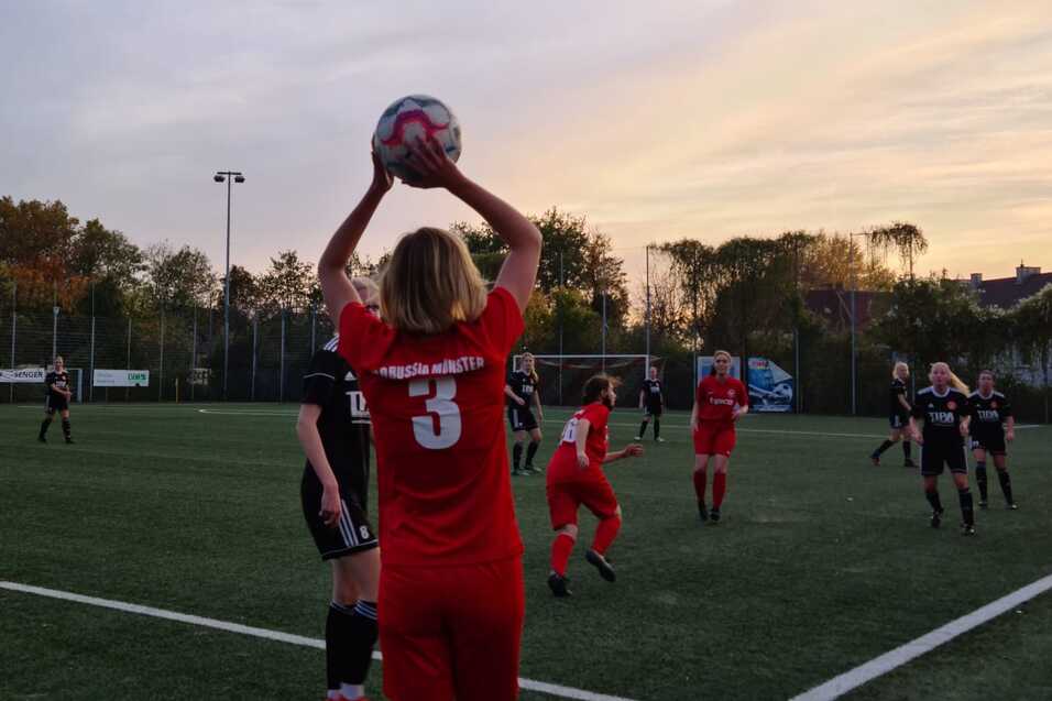 Spielerin in rotem Trikot f&uuml;hrt Einwurf mit Ball auf einem Fu&szlig;ballfeld bei Sonnenuntergang aus, andere Spieler in der N&auml;he.