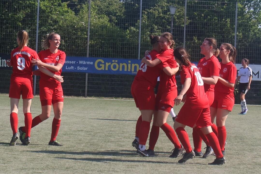 Mehrere Fu&szlig;ballspielerinnen in roten Trikots feiern gemeinsam ein Tor auf einem Rasenplatz.