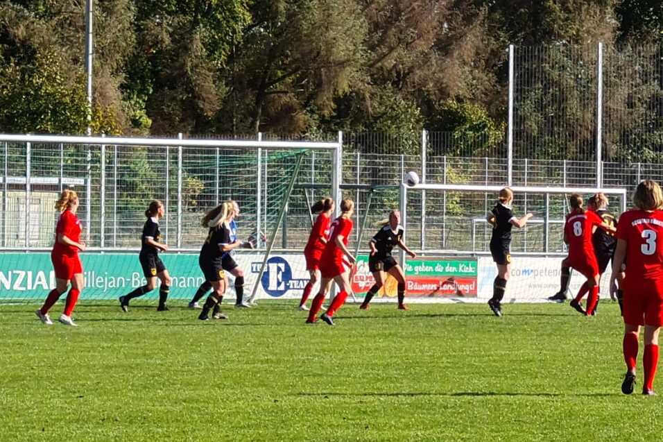 Fu&szlig;ballspiel mit Spielern in roten und schwarzen Trikots auf einem gr&uuml;nen Rasenplatz unter blauem Himmel.