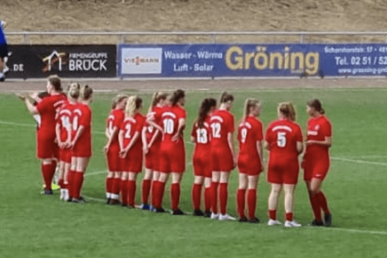 Eine Frauenfu&szlig;ballmannschaft in roten Trikots steht auf dem Platz und bereitet sich auf das Spiel vor.