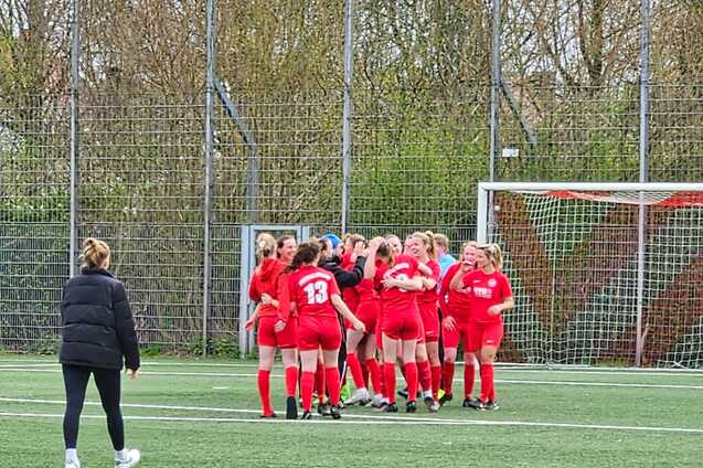Gruppe junger M&auml;dchen in roten Fu&szlig;balltrikots feiert auf dem Spielfeld gemeinsam einen Torerfolg.