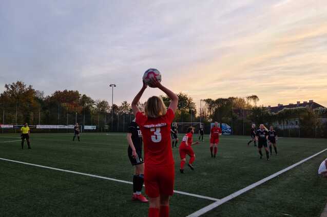 Spielerin in rotem Trikot f&uuml;hrt Einwurf mit Ball auf einem Fu&szlig;ballfeld bei Sonnenuntergang aus, andere Spieler in der N&auml;he.