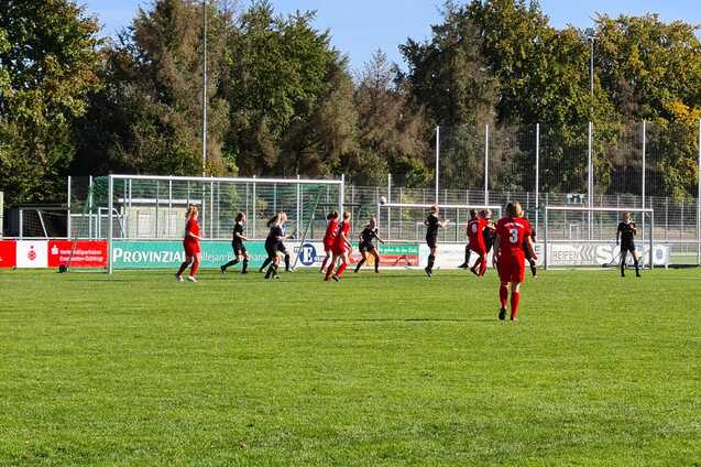 Fu&szlig;ballspiel mit Spielern in roten und schwarzen Trikots auf einem gr&uuml;nen Rasenplatz unter blauem Himmel.