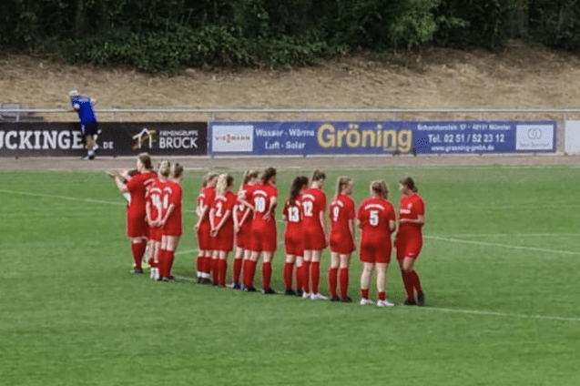 Eine Frauenfu&szlig;ballmannschaft in roten Trikots steht auf dem Platz und bereitet sich auf das Spiel vor.