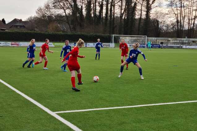 M&auml;dchenfu&szlig;ballspiel auf einem Kunstrasenplatz mit Spielerinnen in roten und blauen Trikots, aktiv am Ball.