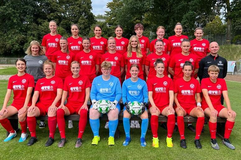 Gruppenfoto der Fu&szlig;ballmannschaft in roten Trikots, bestehend aus 20 Spielerinnen und zwei Torwartinnen auf dem Rasen.
