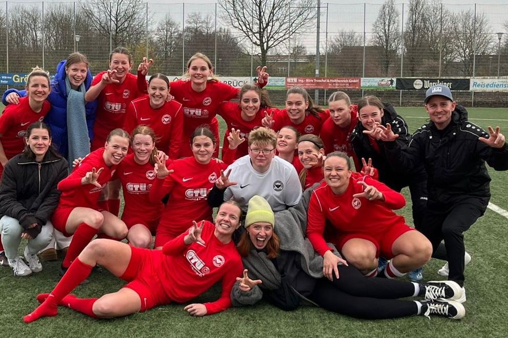 Gruppe von Frauenfu&szlig;ballspielerinnen in roten Trikots posiert fr&ouml;hlich nach einem Spiel auf einem Soccerfeld.