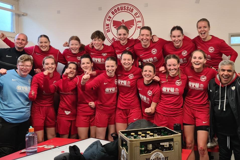 Gruppe von Frauen in roten Sporttrikots posiert freudig in der Umkleidekabine nach dem Spiel.