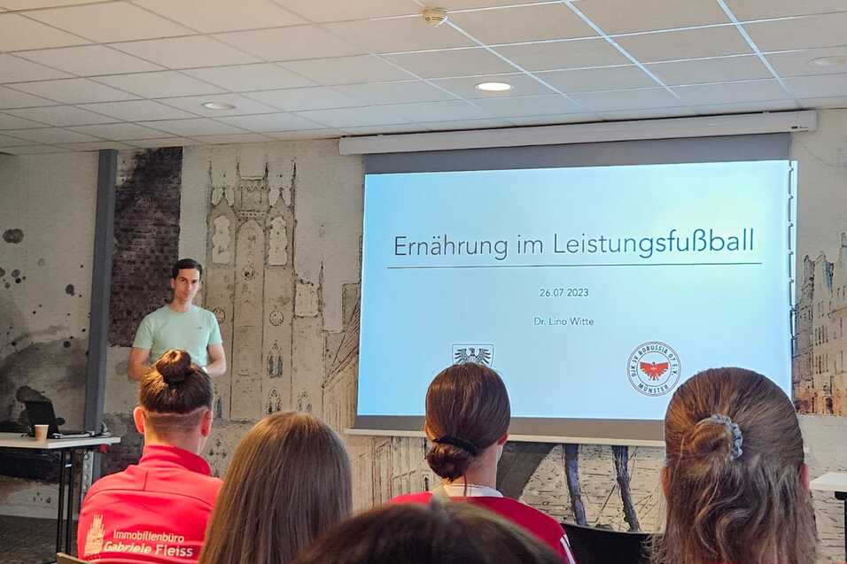 Mann pr&auml;sentiert zum Thema &bdquo;Ern&auml;hrung im Leistungssport&ldquo; vor Publikum in einem modernen Seminarraum.