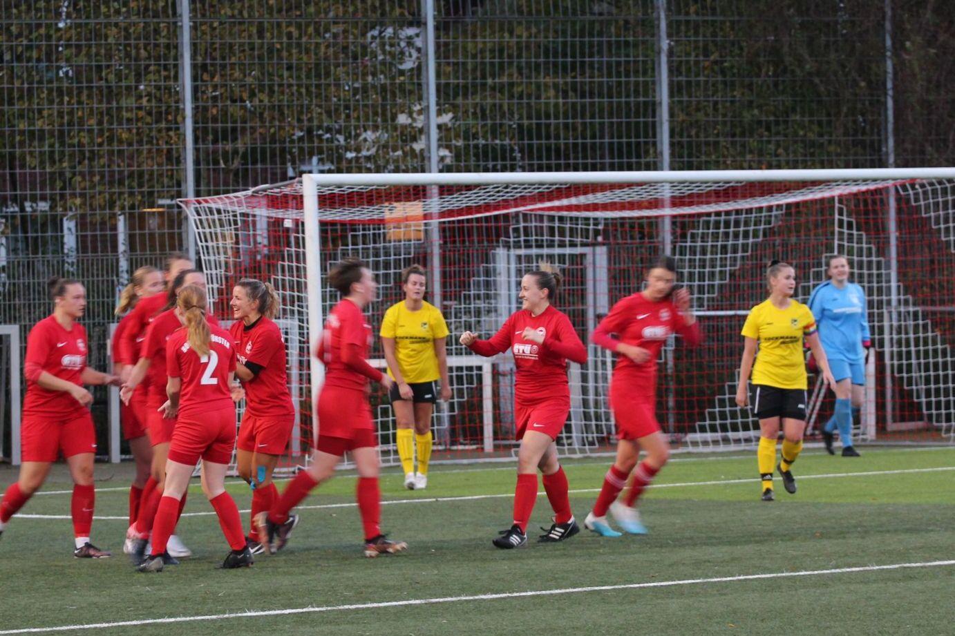 Feiernde Fu&szlig;ballspielerinnen in roten Trikots nach einem Tor, mit einer Torh&uuml;terin in Gelb im Hintergrund.