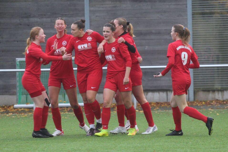 Mannschaft von Frauen in roten Trikots jubelt auf einem Fu&szlig;ballfeld nach einem Torerfolg.