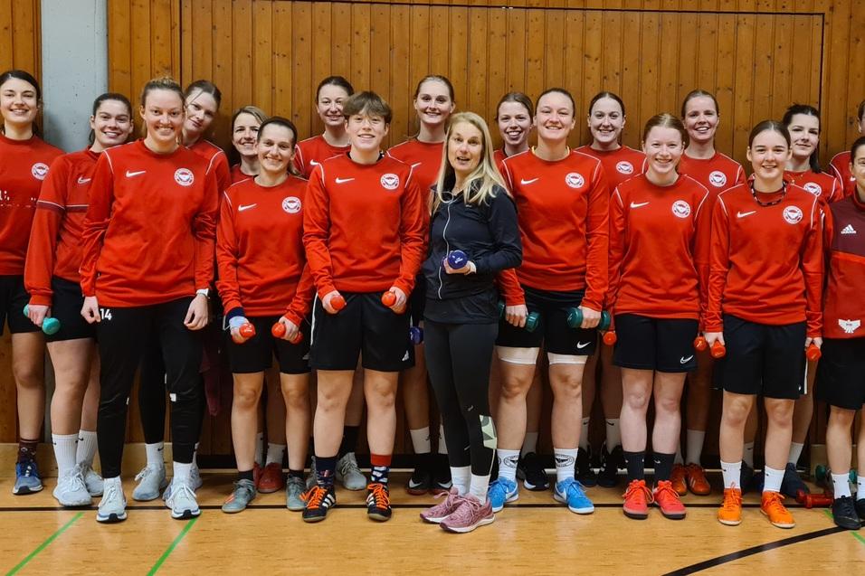 Gruppenfoto von 15 Frauen in roten Trainingsjacken mit Hanteln in der Hand, posing in einer Sporthalle.