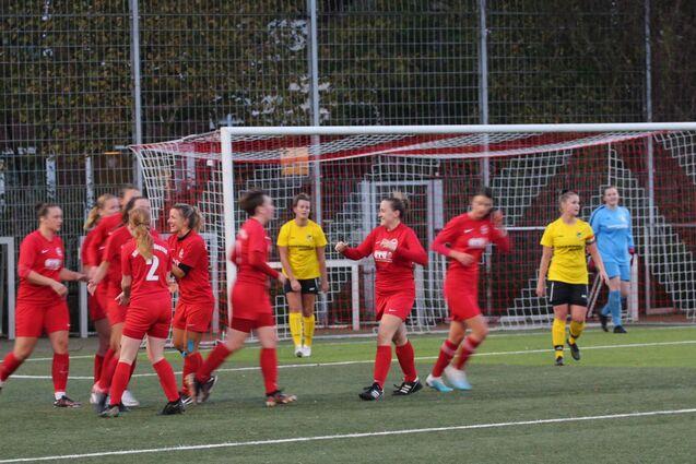 Feiernde Fu&szlig;ballspielerinnen in roten Trikots nach einem Tor, mit einer Torh&uuml;terin in Gelb im Hintergrund.