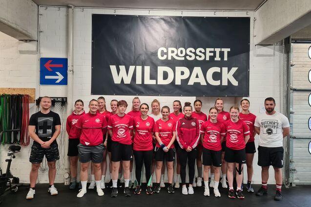 Gruppe von CrossFit-Sportlern in roten Shirts posiert vor einer Wand mit dem Schriftzug &bdquo;CROSSFIT WILDPACK&ldquo;.