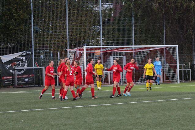 Feiernde Fu&szlig;ballspielerinnen in roten Trikots nach einem Tor, mit einer Torh&uuml;terin in Gelb im Hintergrund.