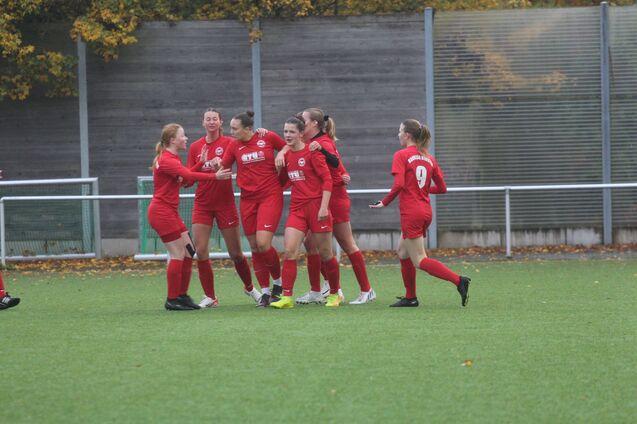 Mannschaft von Frauen in roten Trikots jubelt auf einem Fu&szlig;ballfeld nach einem Torerfolg.