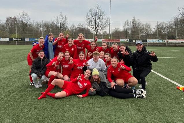 Gruppe von Frauenfu&szlig;ballspielerinnen in roten Trikots posiert fr&ouml;hlich nach einem Spiel auf einem Soccerfeld.
