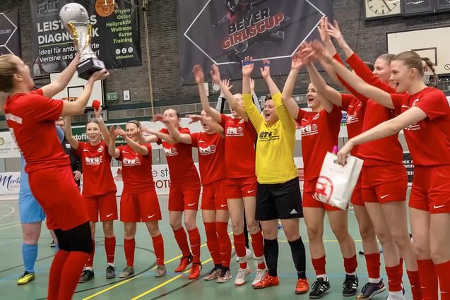 Frauenfu&szlig;ballmannschaft jubelt und feiert mit Pokal in der Sporthalle nach einem gewonnenen Turnier.