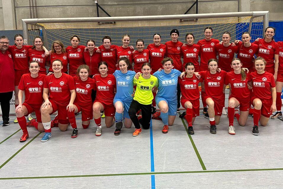 Gruppenfoto einer Frauenfu&szlig;ballmannschaft in roten Trikots mit Trainer, auf einem Hallenfu&szlig;ballfeld posierend.