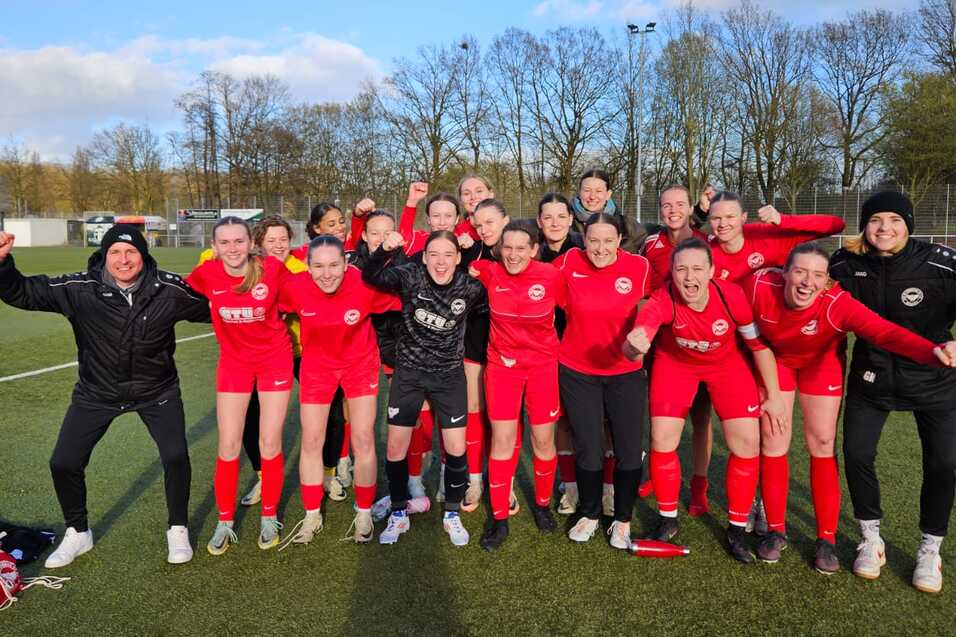 Gruppenzusammenstellung von Frauenfu&szlig;ballspielerinnen in roten Trikots, die jubelnd auf einem Platz posieren.
