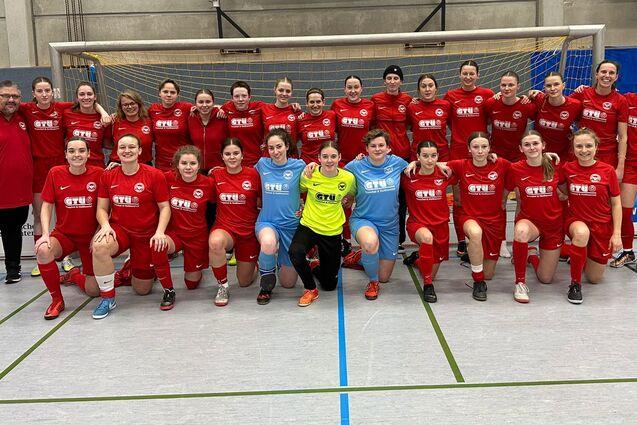 Gruppenfoto einer Frauenfu&szlig;ballmannschaft in roten Trikots mit Trainer, auf einem Hallenfu&szlig;ballfeld posierend.