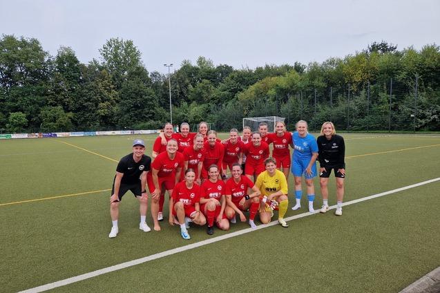 Mannschaftsaufstellung einer Fu&szlig;ballmannschaft in roten Trikots auf einem Kunstrasenplatz, umgeben von B&auml;umen.