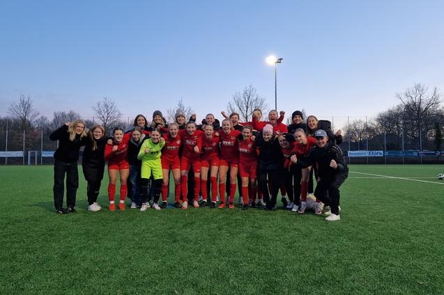 Gruppenshot einer Frauenfu&szlig;ballmannschaft in roten Trikots, umgeben von Unterst&uuml;tzern auf einem Kunstrasenplatz.