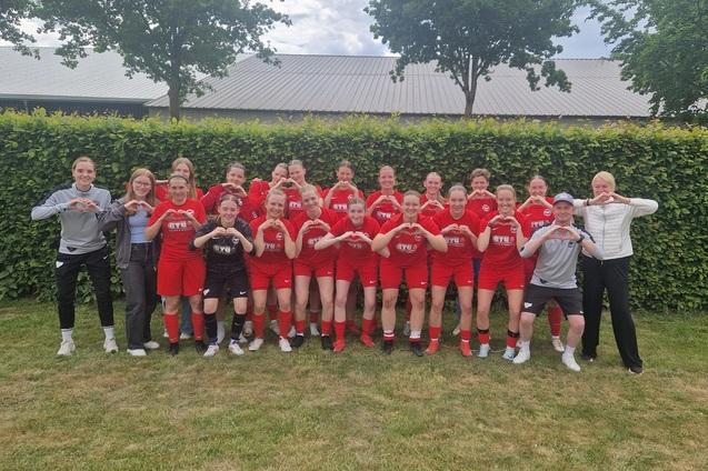 Gruppenzusammenstellung von Frauenfu&szlig;ballspielerinnen in roten Trikots, posierend vor einer gr&uuml;nen Hecke.