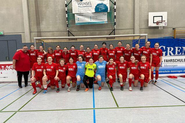 Gruppenfoto einer Frauenfu&szlig;ballmannschaft in roten Trikots mit Trainer, auf einem Hallenfu&szlig;ballfeld posierend.
