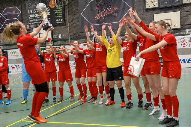 Frauenfu&szlig;ballmannschaft jubelt und feiert mit Pokal in der Sporthalle nach einem gewonnenen Turnier.