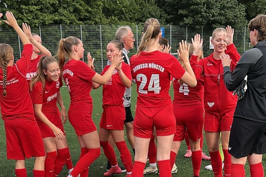 M&auml;dchenfu&szlig;ballmannschaft in roten Trikots feiert jubelnd auf dem Spielfeld nach einem Erfolg.