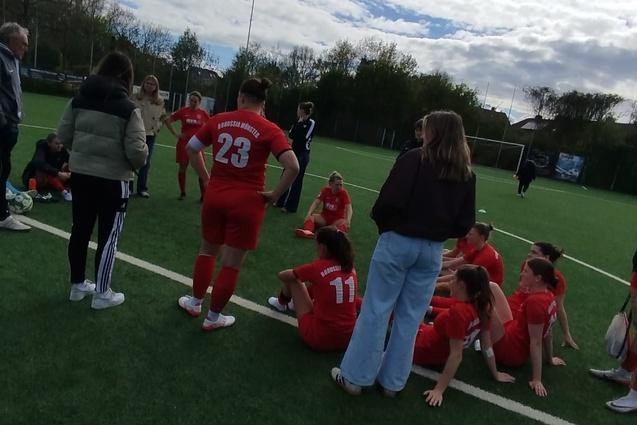 Gruppe von Fu&szlig;ballspielerinnen in roten Trikots auf dem Rasenplatz, w&auml;hrend sie sich nach dem Spiel versammeln.