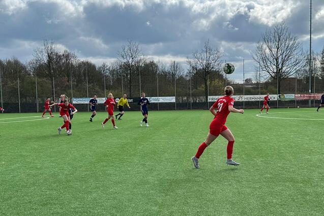 Spielszene auf einem Kunstrasenplatz mit Spielern in roten Trikots, die den Ball verfolgen und dem Spielgeschehen Aufmerksamkeit schenken.