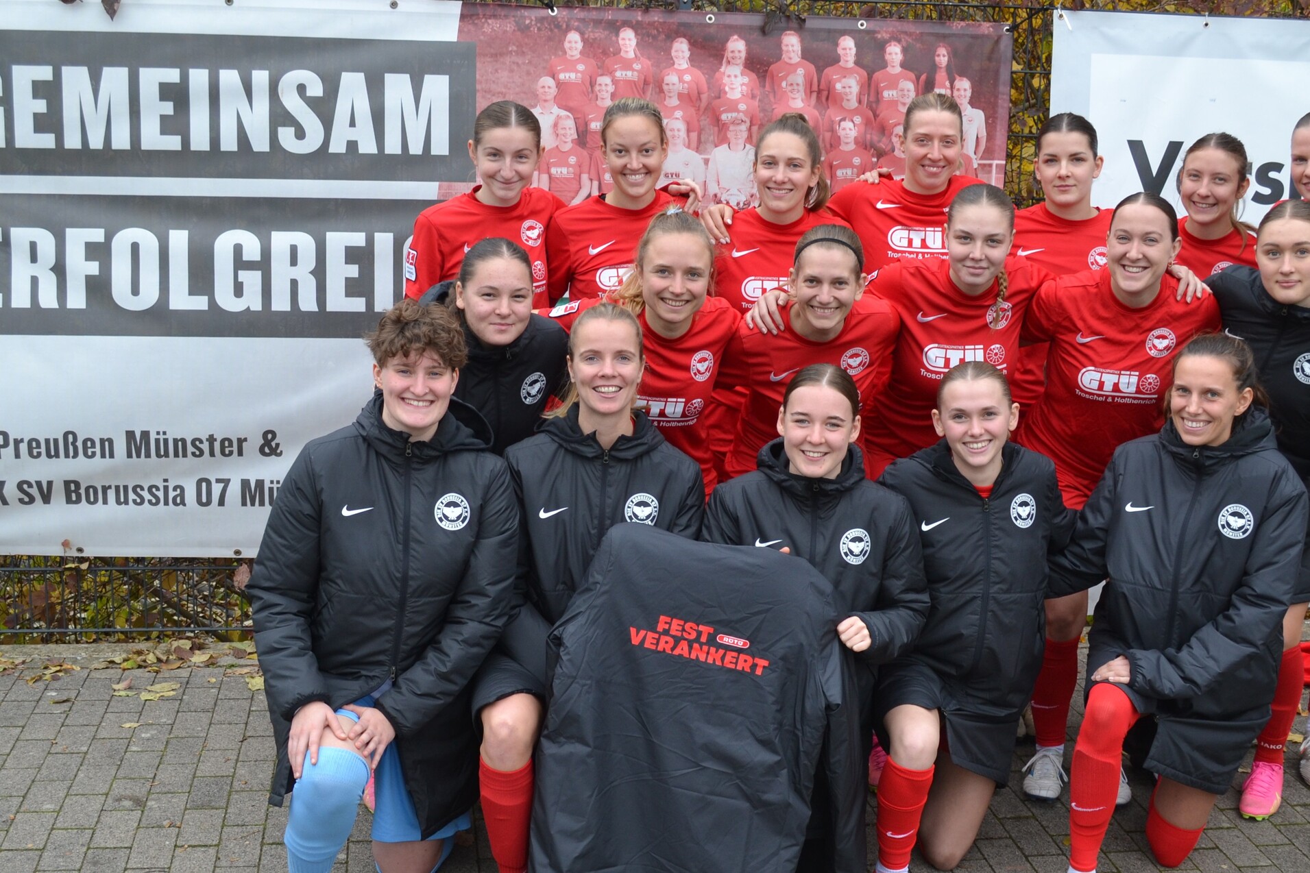 Gruppenfoto von Fu&szlig;ballspielerinnen in roten Trikots, die vor einem Banner mit der Aufschrift &bdquo;Gemeinsam Erfolgreich&ldquo; stehen.