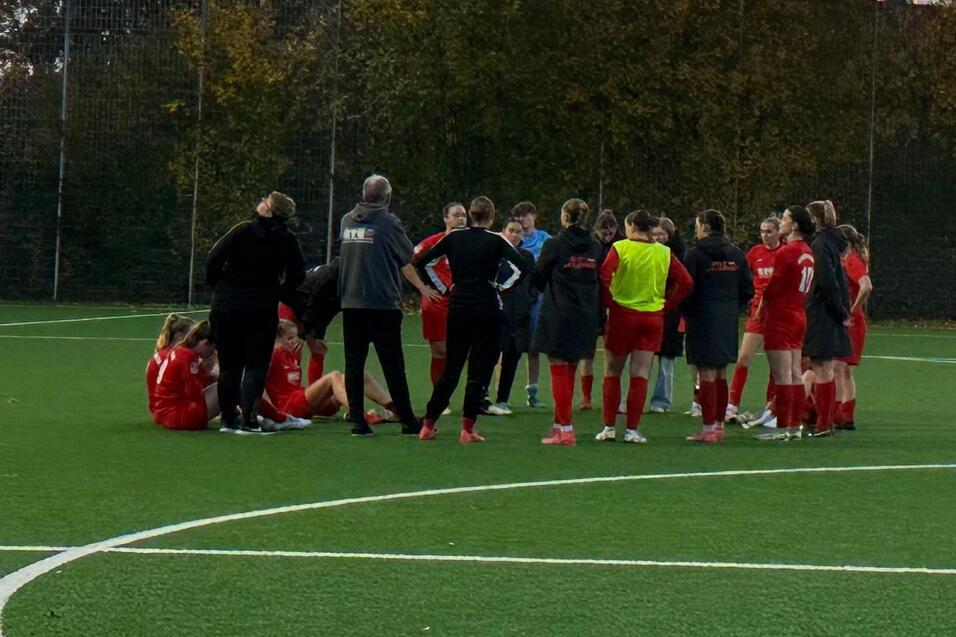 Gruppe von Fu&szlig;ballspielern in roten Trikots versammelt sich bei Sonnenuntergang auf einem Kunstrasenplatz.