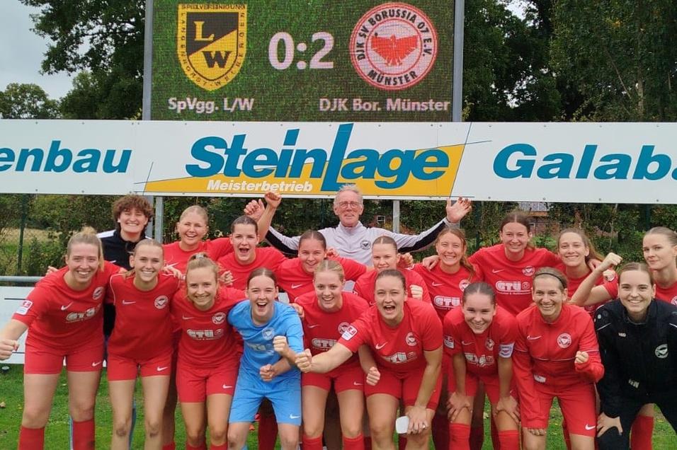 Feiernde Frauenfu&szlig;ballmannschaft in roten Trikots posiert nach dem Spiel vor einer Anzeigentafel.
