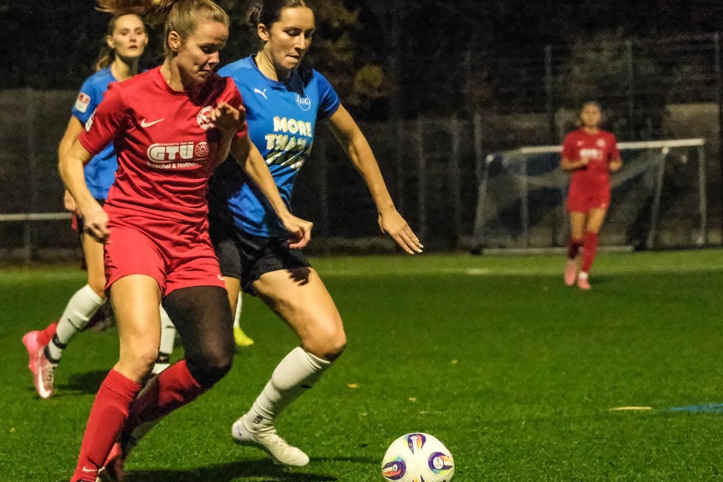 Zwei Fu&szlig;ballspielerinnen in Aktion auf einem Kunstrasenplatz, mit einem Ball zwischen ihnen.