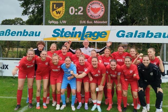 Feiernde Frauenfu&szlig;ballmannschaft in roten Trikots posiert nach dem Spiel vor einer Anzeigentafel.