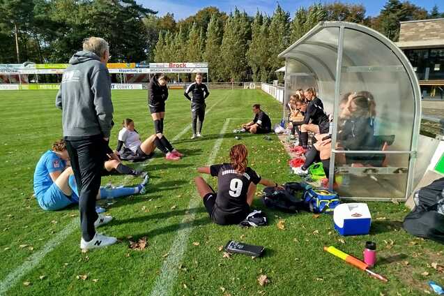 Sitzende und stehende Fu&szlig;ballspielerinnen besprechen sich auf einer Rasenfl&auml;che neben einer Trainerbank.