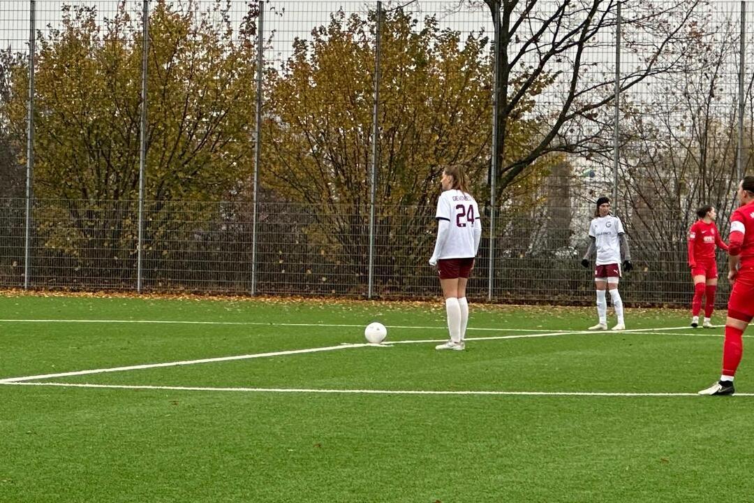 Frauenfu&szlig;ballspiel auf Kunstrasen, Spielerinnen in roten und wei&szlig;en Trikots, Ball liegt zum Ansto&szlig; bereit.